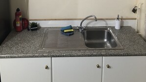 A kitchen with a granite countertop, a stainless steel sink, and a red decorative piece above it.