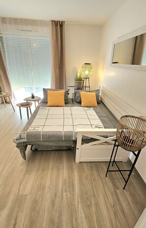 A modern bedroom with a bed, two bedside tables, a small table, a lamp, and a mirror.