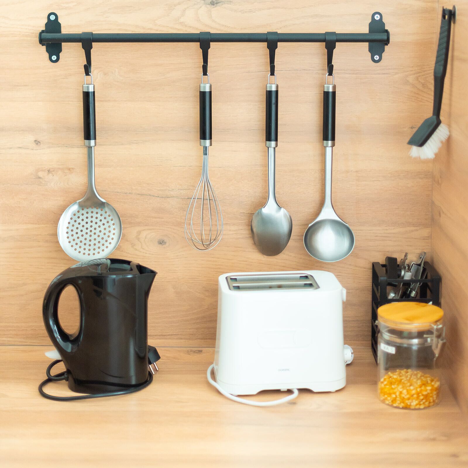 Een keuken met een hangende rek met keukengerei, een koffiezetapparaat, een broodrooster en een pot maïskorrels.