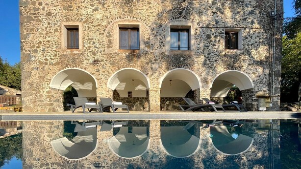 A stone building with a pool and lounge chairs.