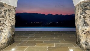 An arched stone pathway leading to a balcony with a view of a sunset over mountains.