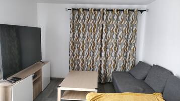 Una sala de estar moderna con un televisor de pantalla plana, un sofá, una mesa de centro y una cortina estampada.