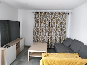 Una sala de estar moderna con un televisor de pantalla plana, un sofá, una mesa de centro y una cortina estampada.