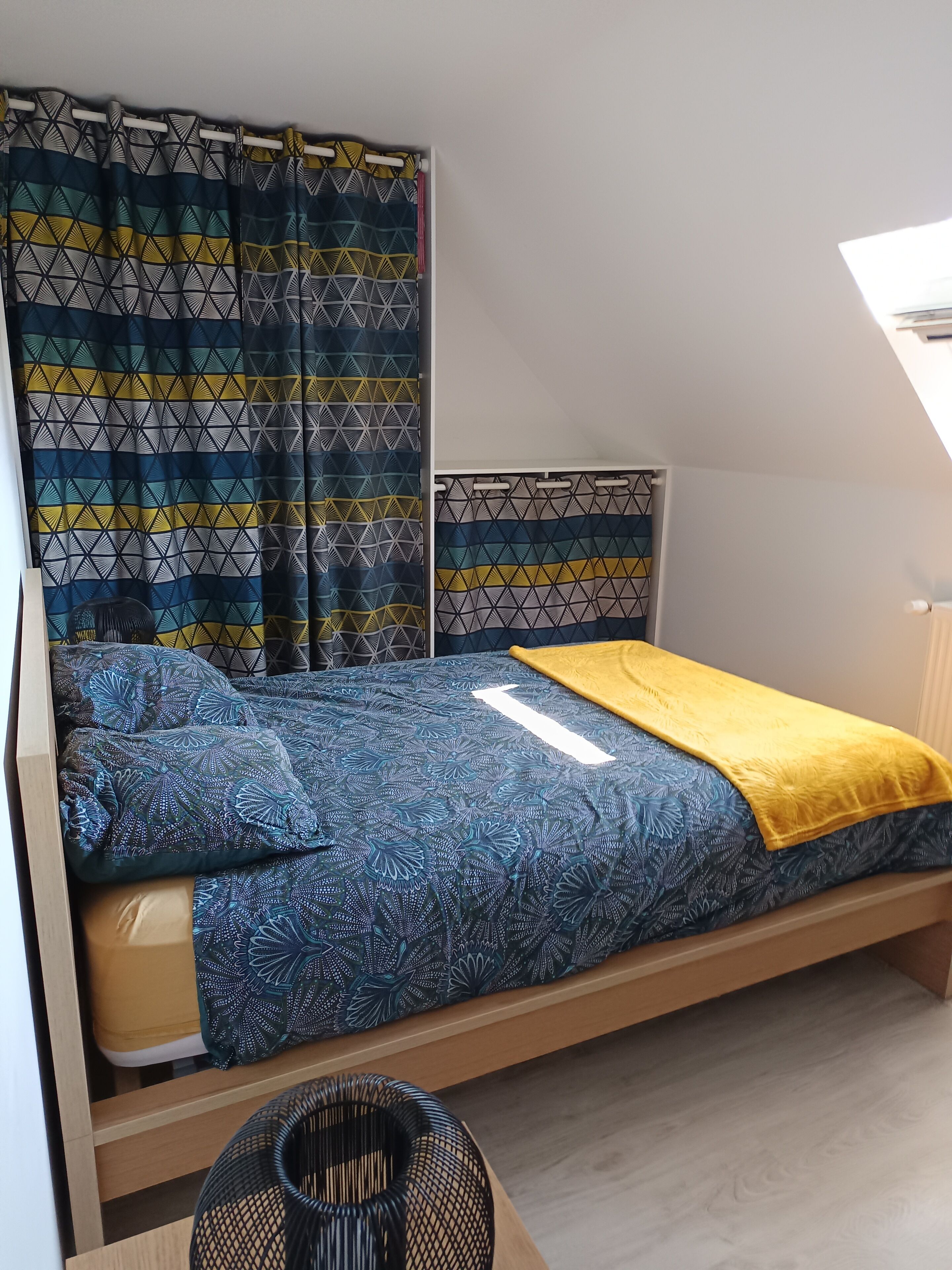 Een eenpersoonsbed met een bedspread met een geometrisch patroon, een gele plaid en een hoofdbord met een geometrisch ontwerp.