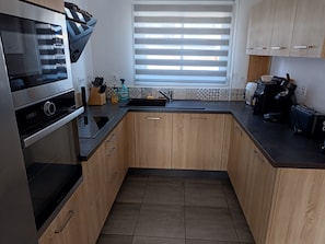 Una cocina moderna con armarios de madera, horno empotrado, cafetera y ventana con persianas.
