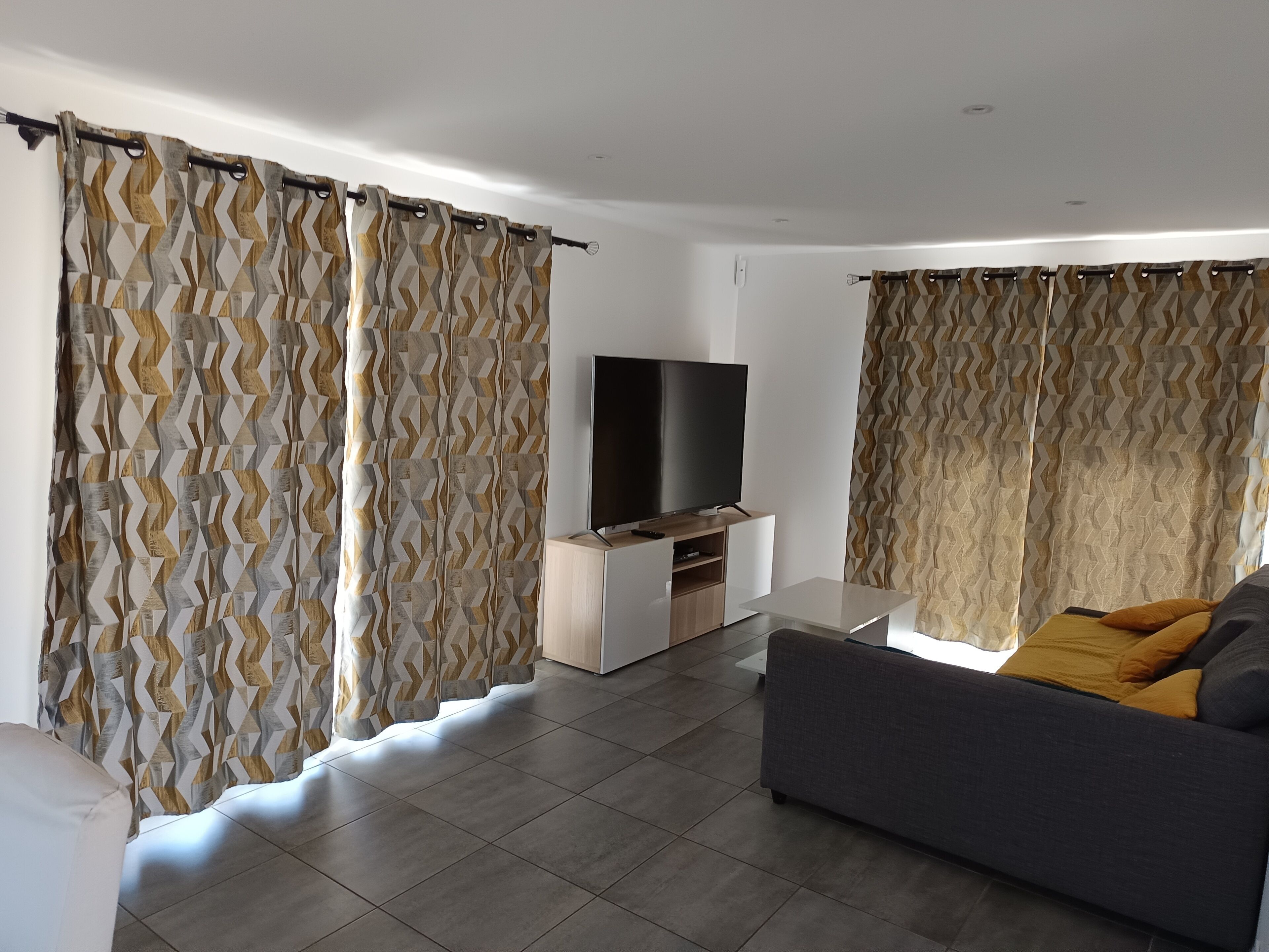 A modern living room with a flat-screen TV, grey sofa, and patterned curtains.