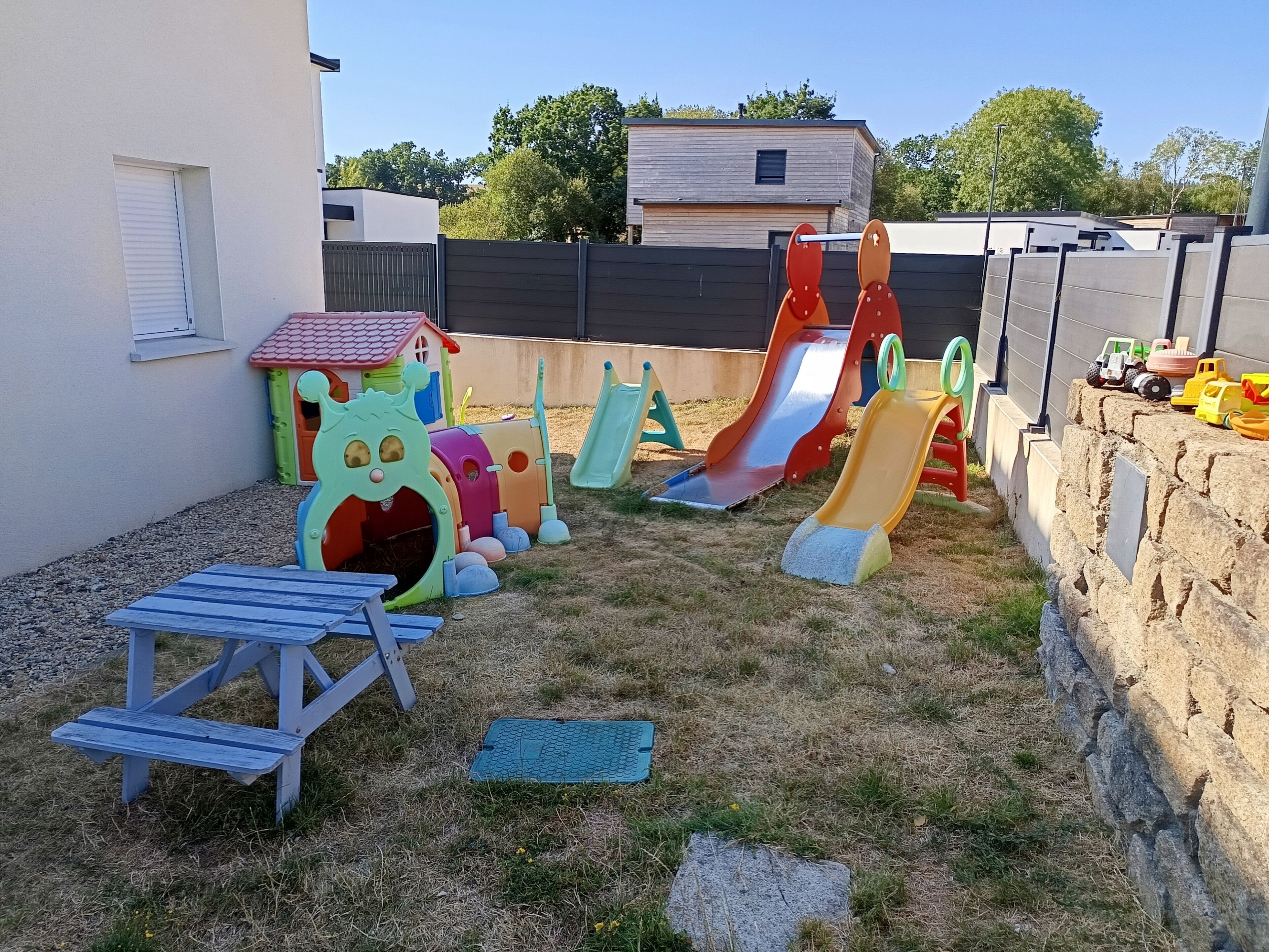 Een achtertuin met een speelruimte, inclusief glijbanen en een poppenhuis.