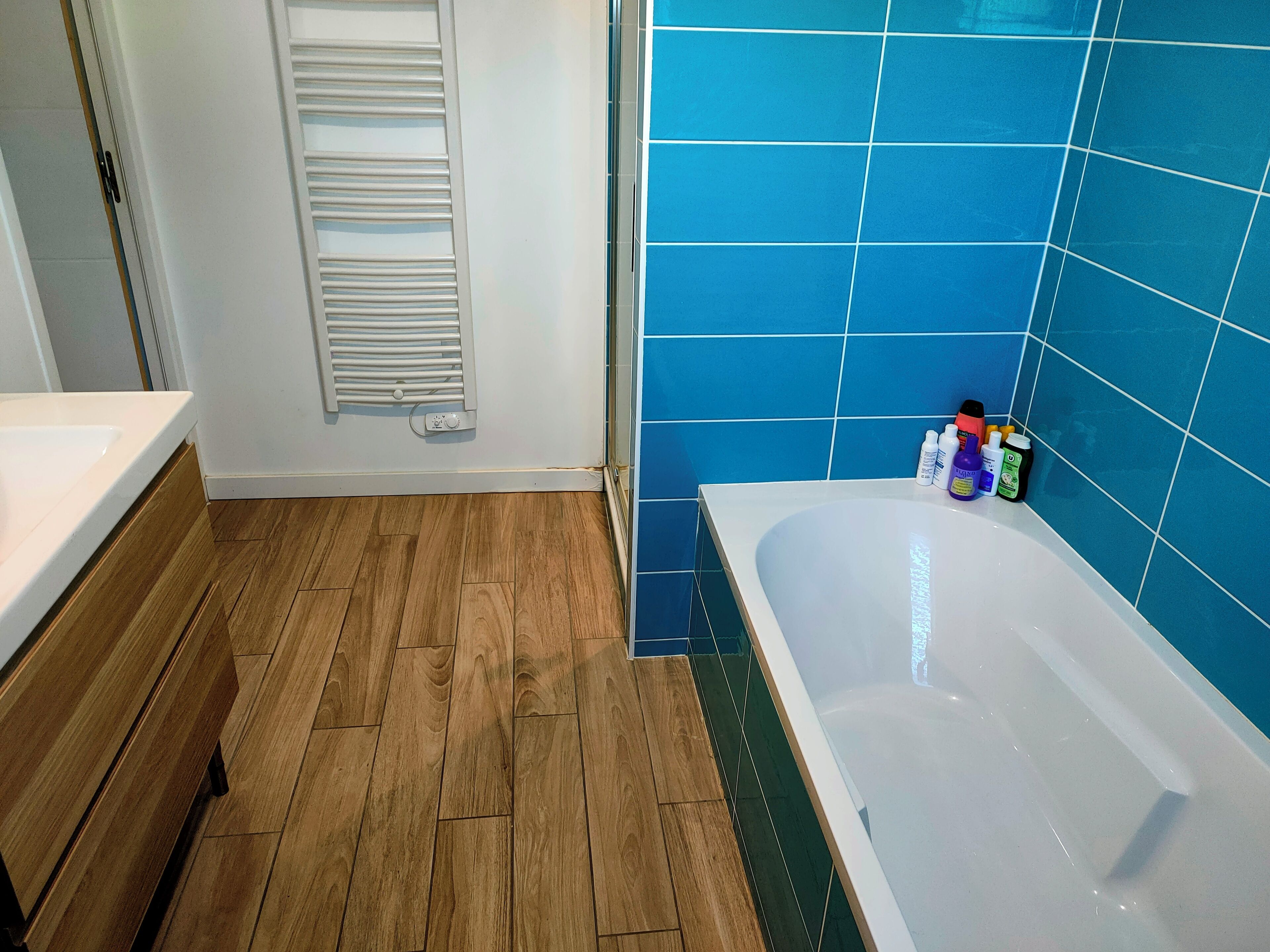 Een badkamer met een houten vloer, een witte badkuip en blauwe tegels op de muur.