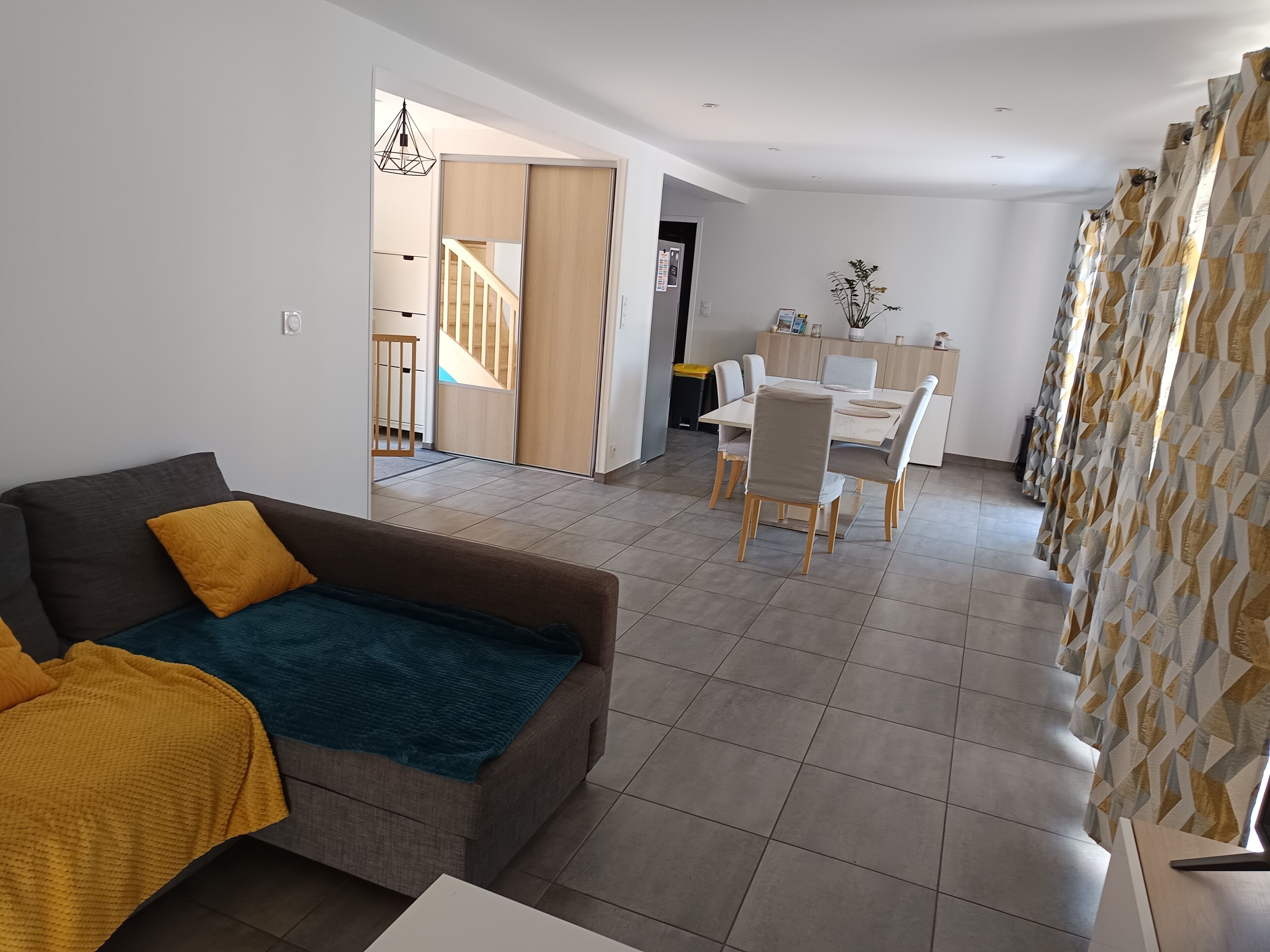 A modern living room with a sofa, a dining area with a table and chairs, and a staircase leading to another level.