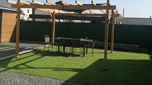 A wooden pergola structure with a table and chairs underneath, surrounded by a well-maintained lawn and gravel path. - Maison Ancienne au Calme (Soulaire-et-Bourg, France)