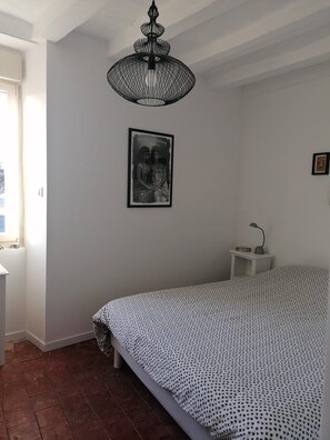Un dormitorio con una cama, un candelabro colgante, un cuadro enmarcado en la pared y una mesita de noche con una lámpara.
