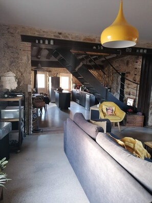 A modern kitchen with a central island, a dining area with a sofa, and a staircase leading to an upper level. - Maison Ancienne au Calme (Soulaire-et-Bourg, France)