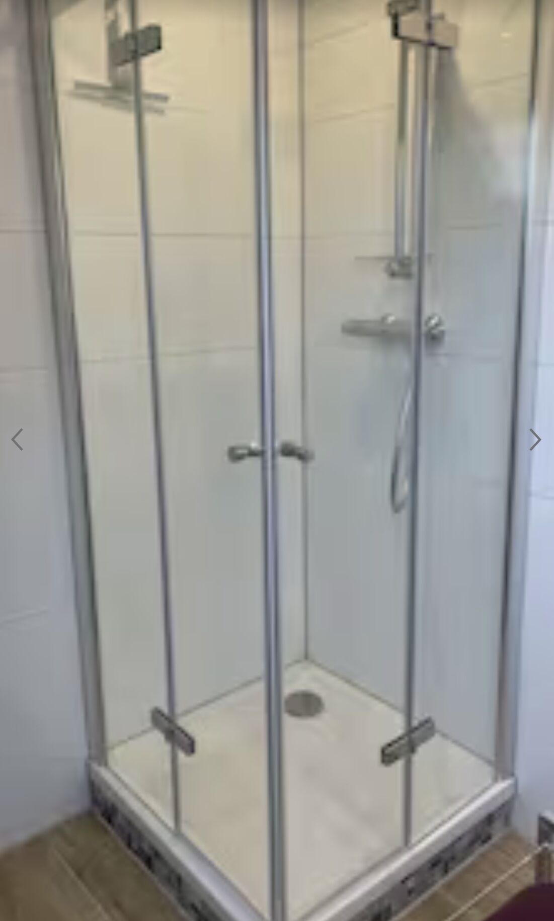 Een douchecabine met glazen wanden, een betegelde vloer en een metalen douchekop.