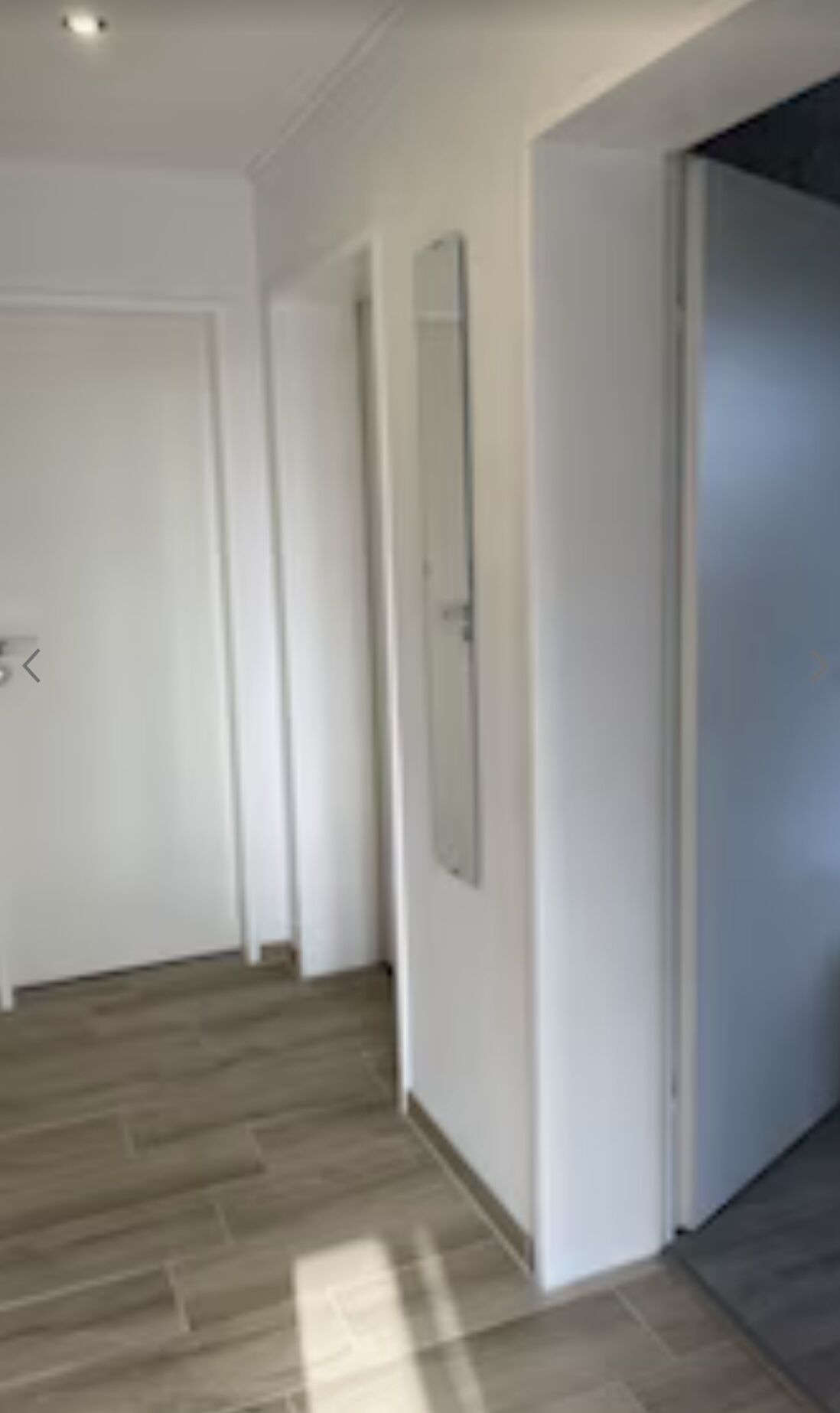 Un couloir avec un plancher en bois, des murs blancs et une porte au fond.