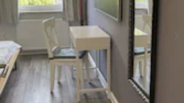 Una habitación con cama, escritorio, silla, ventana con cortinas y un espejo grande en la pared.