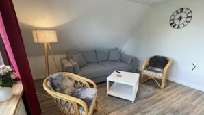 Una sala de estar con un sofá gris, dos sillones de mimbre, una mesa de centro blanca y una lámpara de pie.