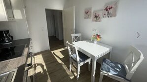 Una cocina compacta con estufa, una mesa de comedor con sillas y un pasillo que conduce a otra habitación.