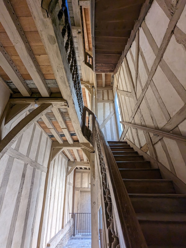 A wooden staircase with a handrail, leading to a room with a wooden ceiling and a window.