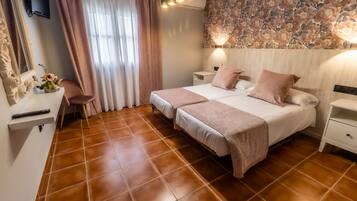 Un dormitorio con dos camas, un escritorio, una silla, un televisor y un papel tapiz floral.