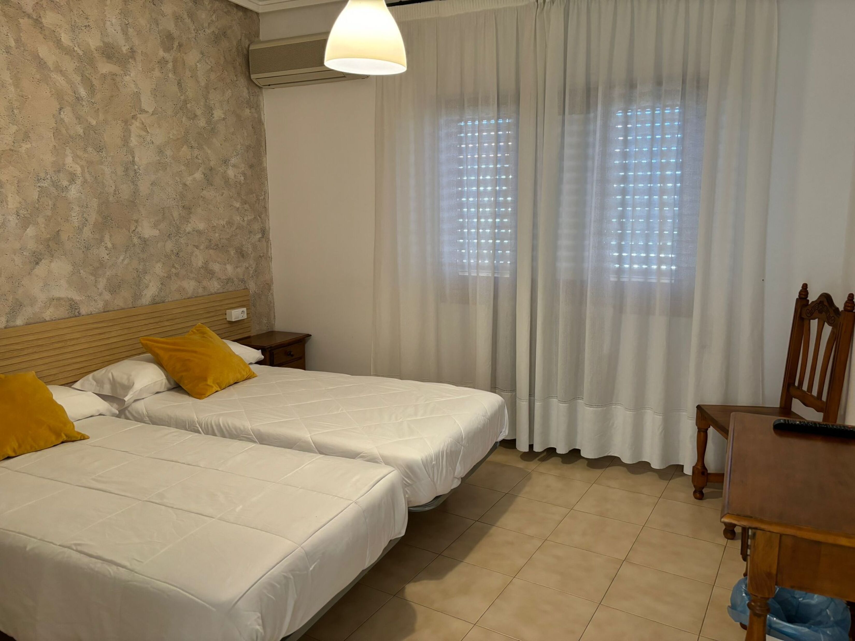 A hotel room with two beds, a wooden headboard, a small bedside table, a desk, and a chair.
