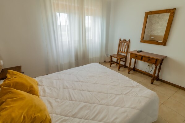 Un dormitorio con una cama, un escritorio de madera, una silla y un espejo en la pared.