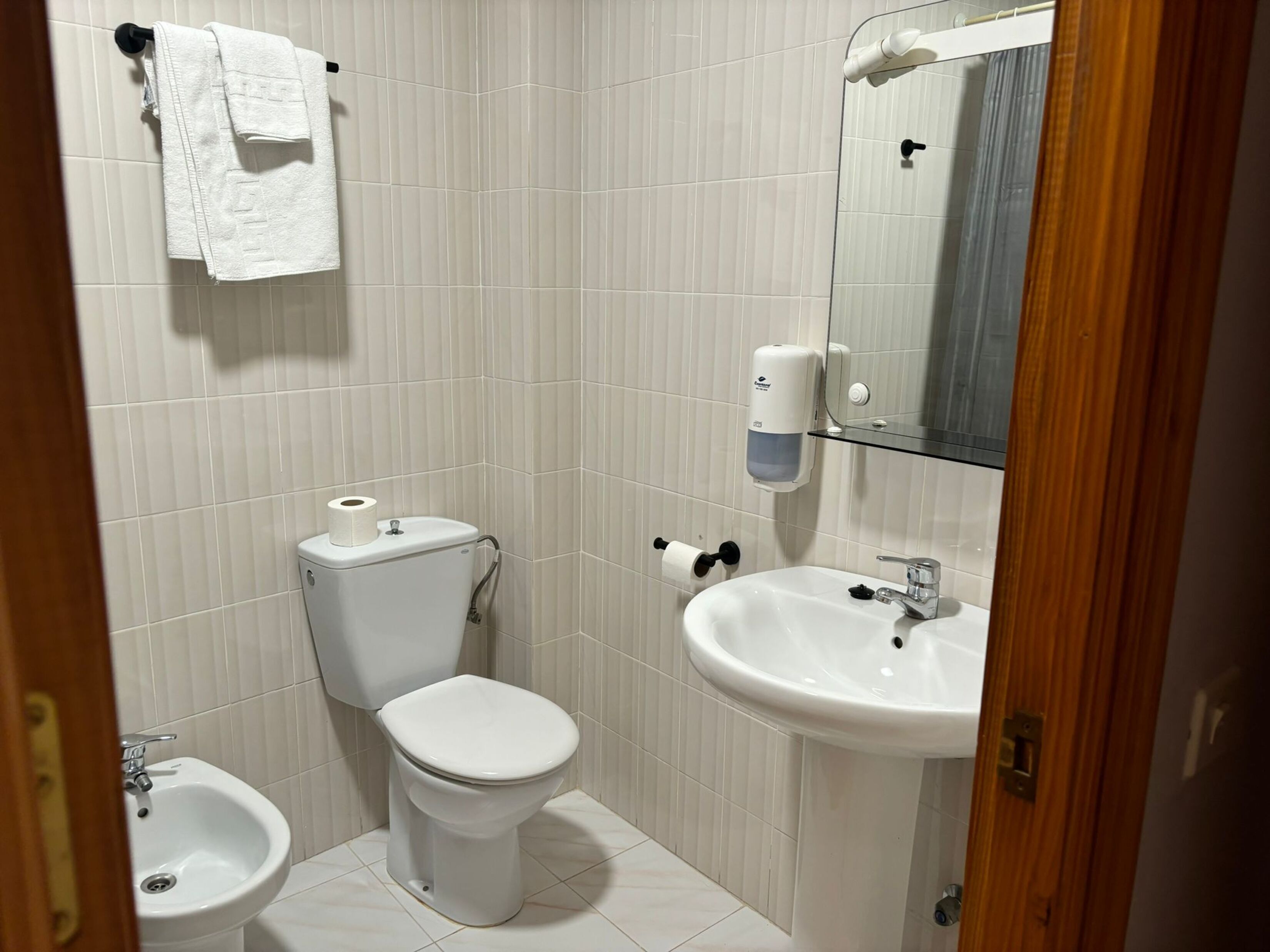 A bathroom with a toilet, bidet, sink, and a towel rack.