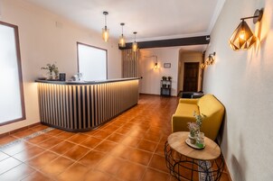 A reception area with a wooden reception desk, a yellow sofa, and a small round table with a vase.
