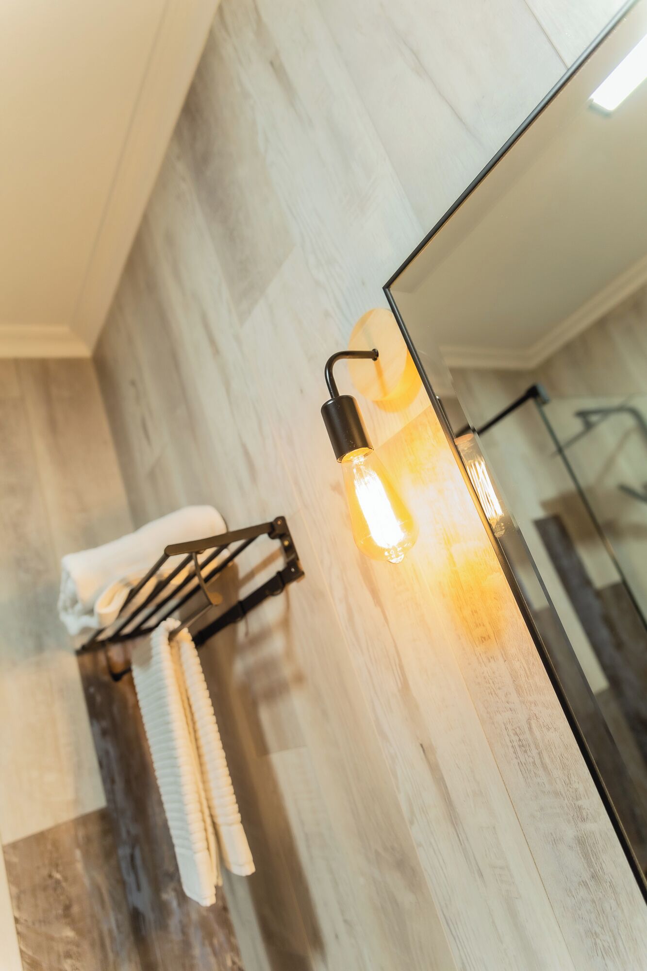 A bathroom with a wooden floor, a towel rack with folded towels, and a wall-mounted light fixture.