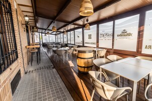 A restaurant with wooden tables and chairs, hanging wicker lamps, and large windows with logos.