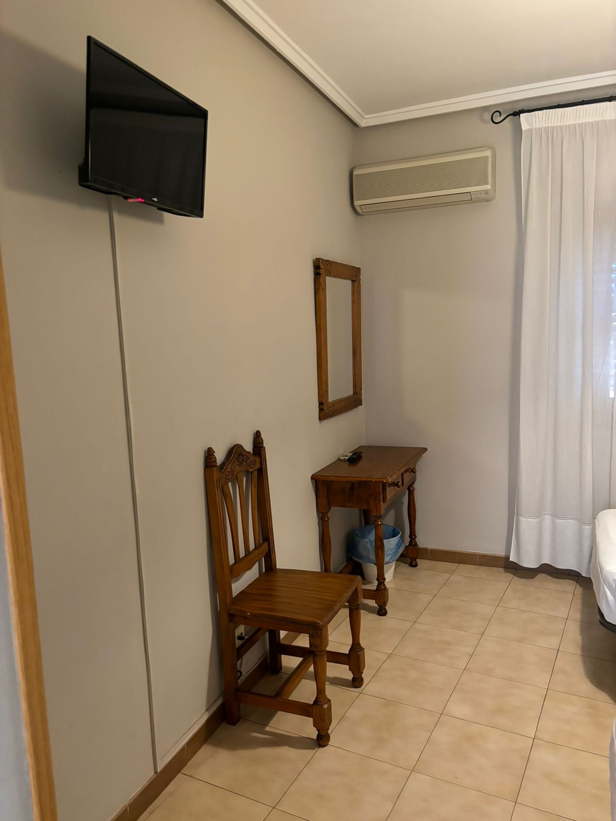 Ein Zimmer mit einem Holzhocker, einem kleinen Tisch, einem an der Wand montierten Fernseher und einer Klimaanlage.
