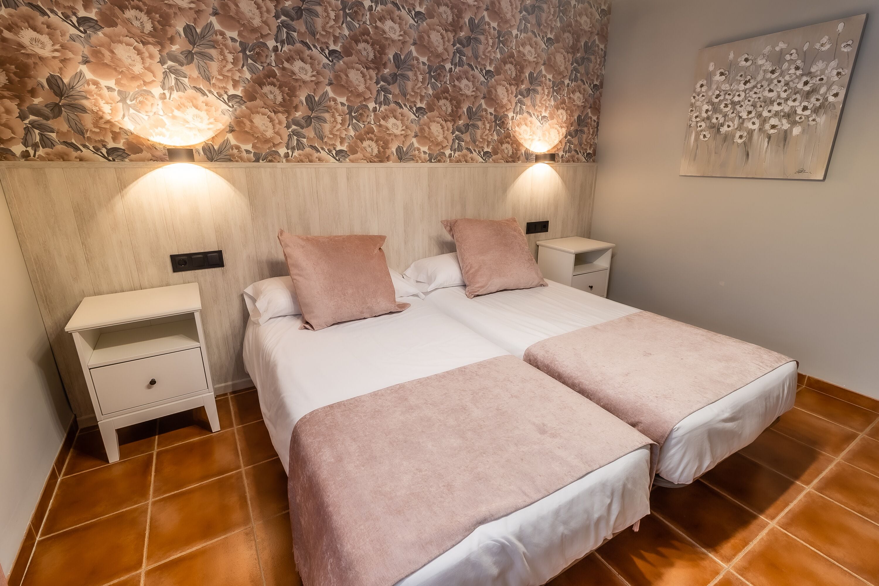 Un letto matrimoniale con due comodini, una lampada a muro e una parete decorata con motivi floreali.