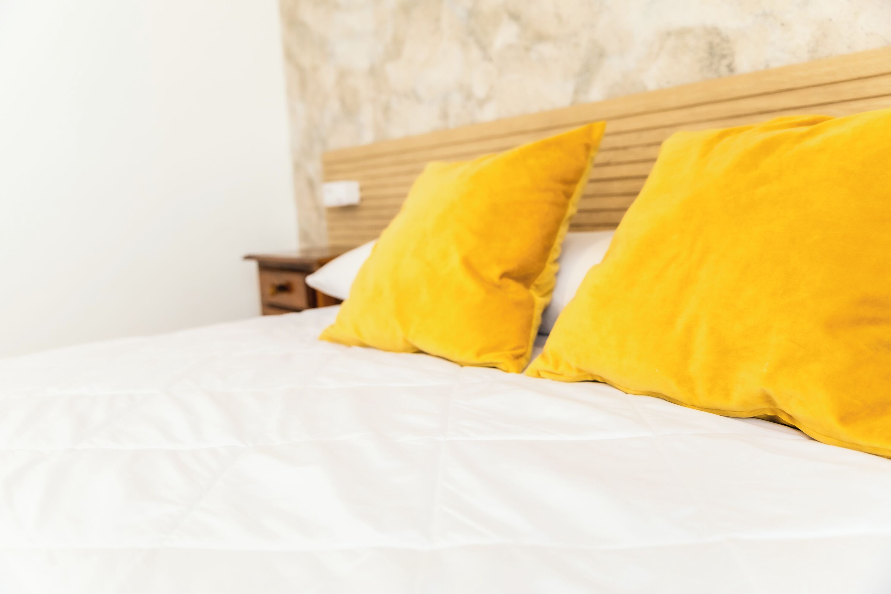 Een bed met witte lakens en twee heldergele kussens.