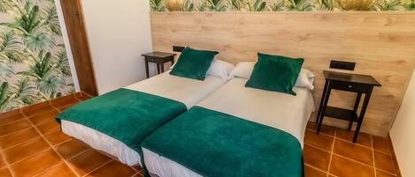 Una cama doble con ropa de cama verde, un cabecero de madera, dos mesitas de noche y una pared con estampado de hojas tropicales.
