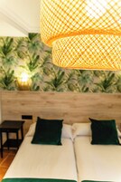 A room with two beds, a wooden headboard, a small table, and a wall with a green leafy pattern.