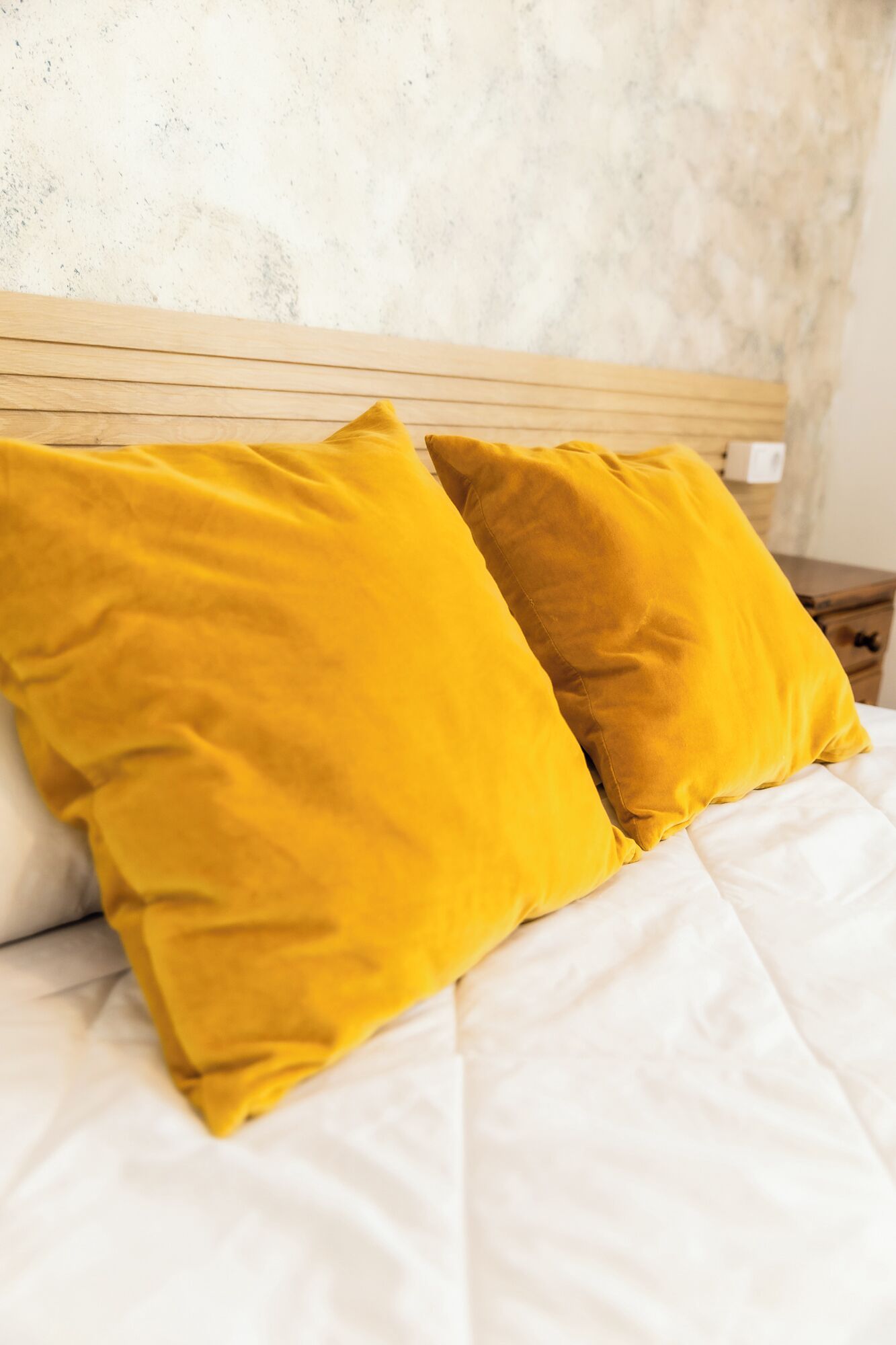 Una cama con ropa de cama blanca y dos almohadas color mostaza.