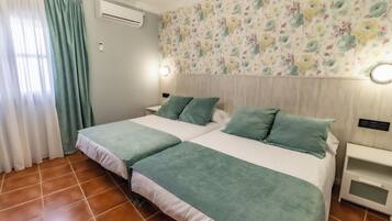 A double bed with green bedding, a nightstand, a wall-mounted air conditioner, and a floral-patterned wallpaper.