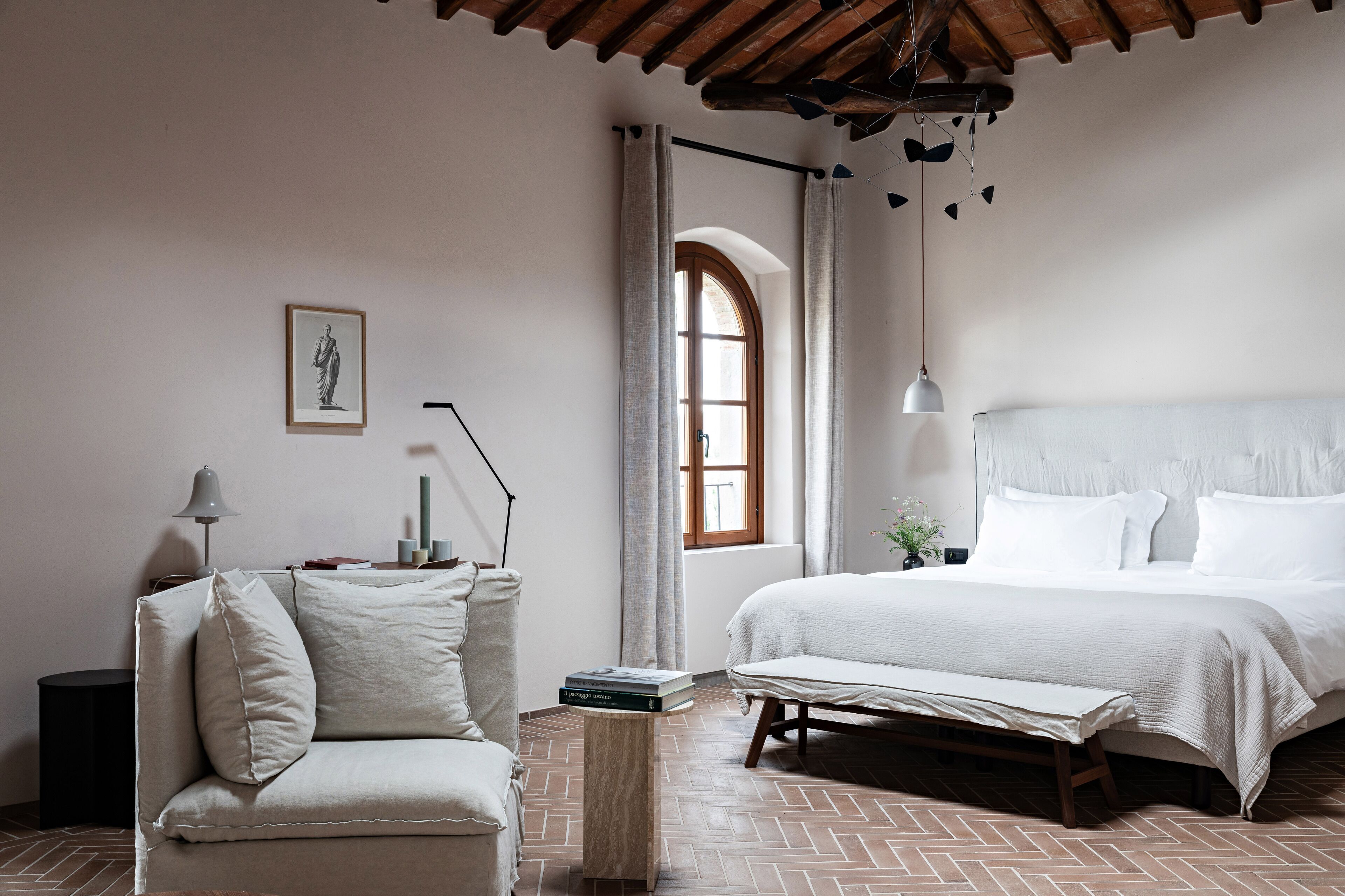 Quarto com cama grande, mesa de cabeceira, cadeira, abajur e janela com cortinas.