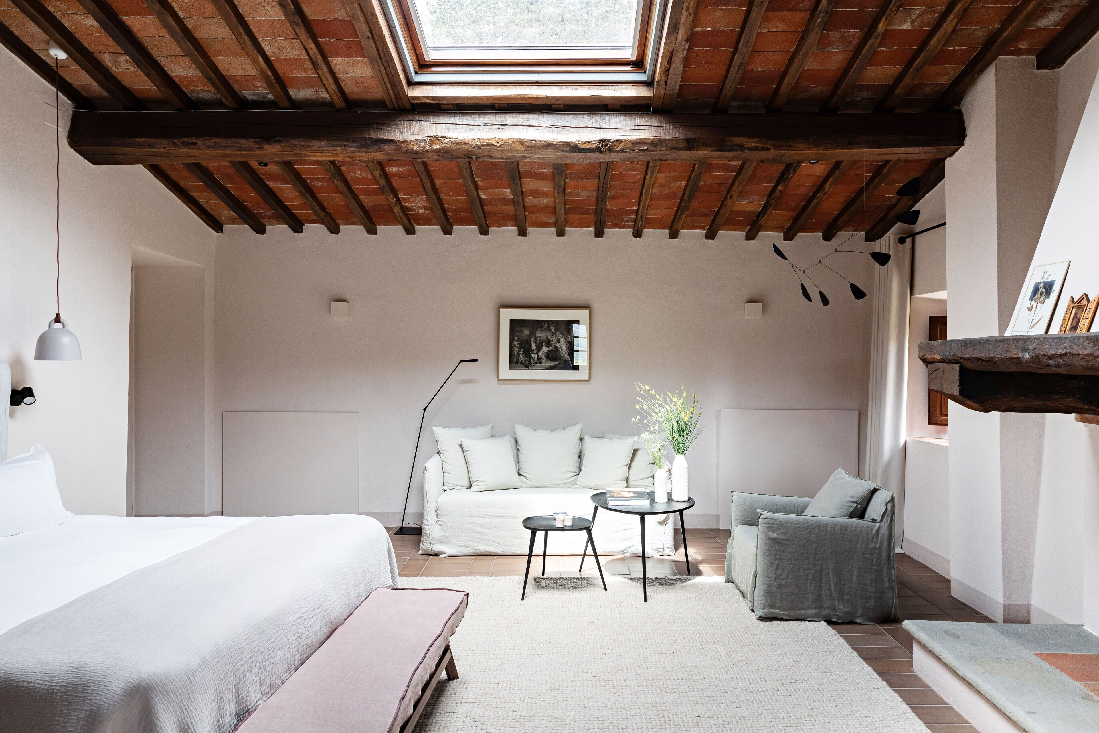 Ein gemütliches Zimmer mit einem Bett, einem Schlafsofa, einem kleinen Tisch und einem Sessel. Über dem Schlafsofa befindet sich ein Oberlicht und ein Bild hängt an der Wand.