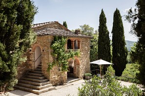 Un edificio de piedra con tejado de baldosas, una escalera que lleva a la entrada y un jardín con una mesa y sillas.