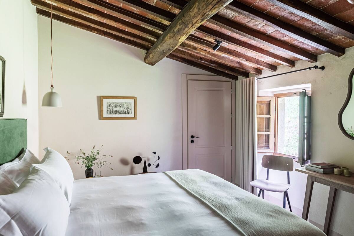 A bedroom with a bed, a desk, a chair, a door, and a window.