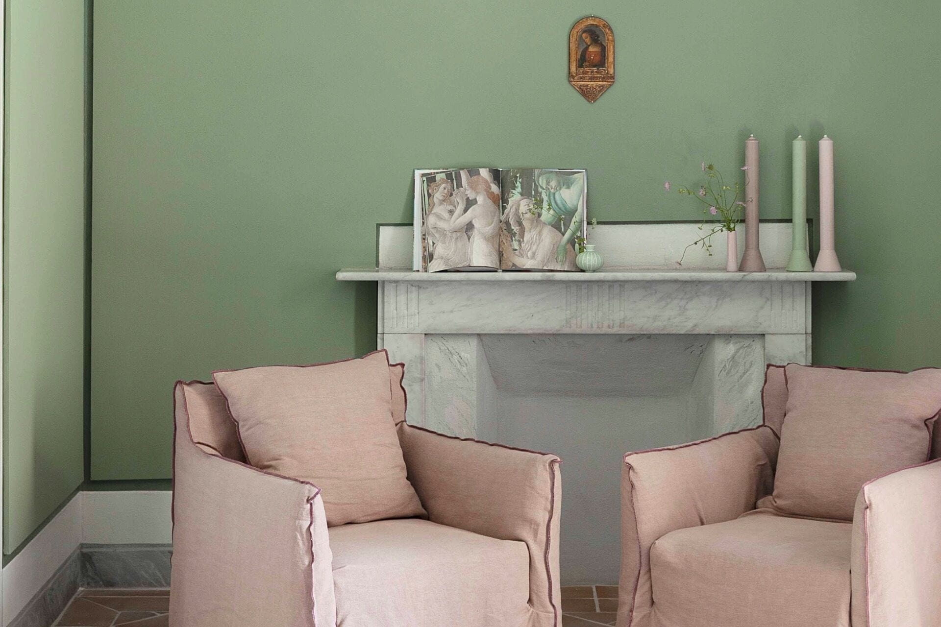 A room with a green wall, a fireplace with a mantel, and two chairs.