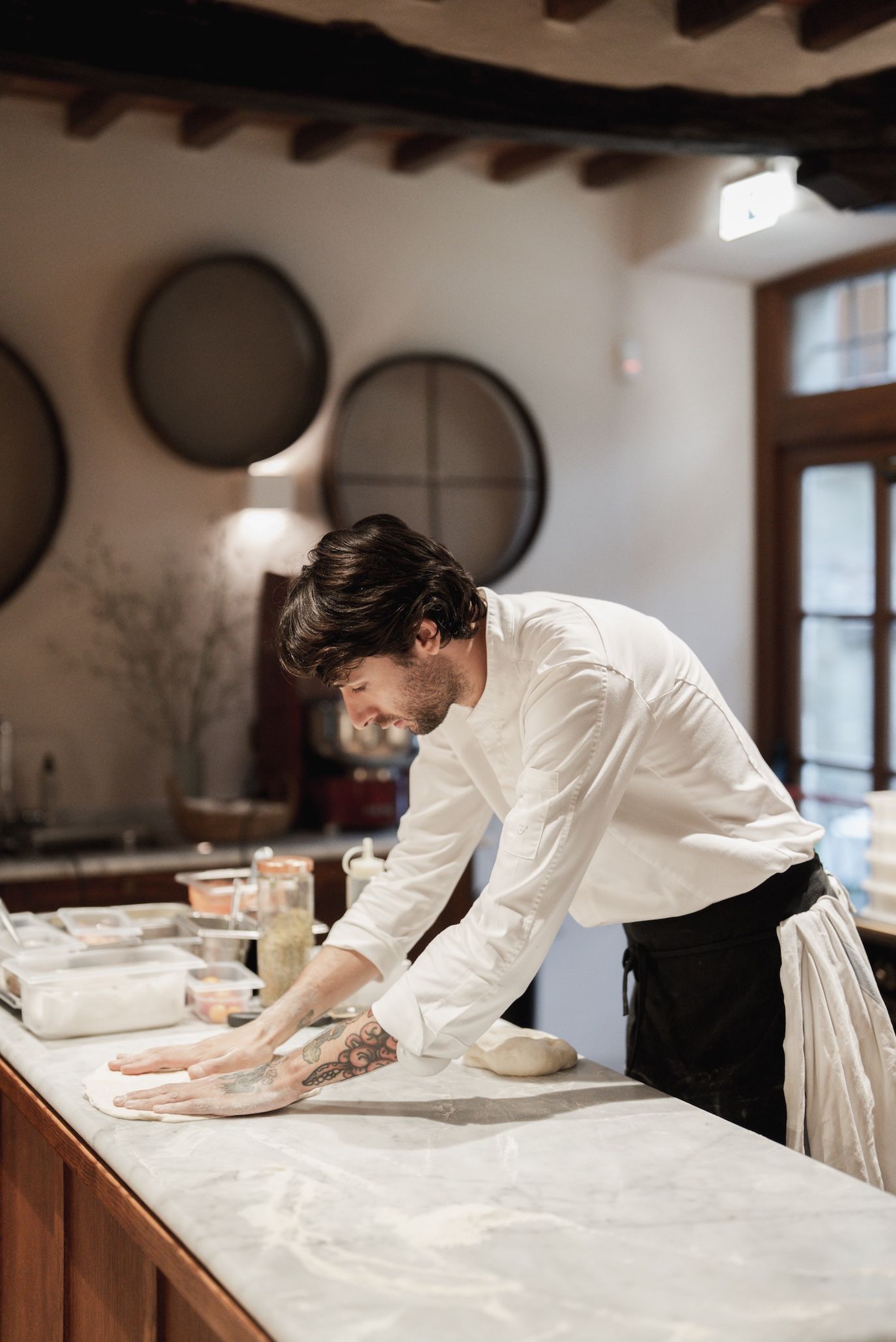 A person working at a marble counter in a kitchen with round wall decorations and a window.