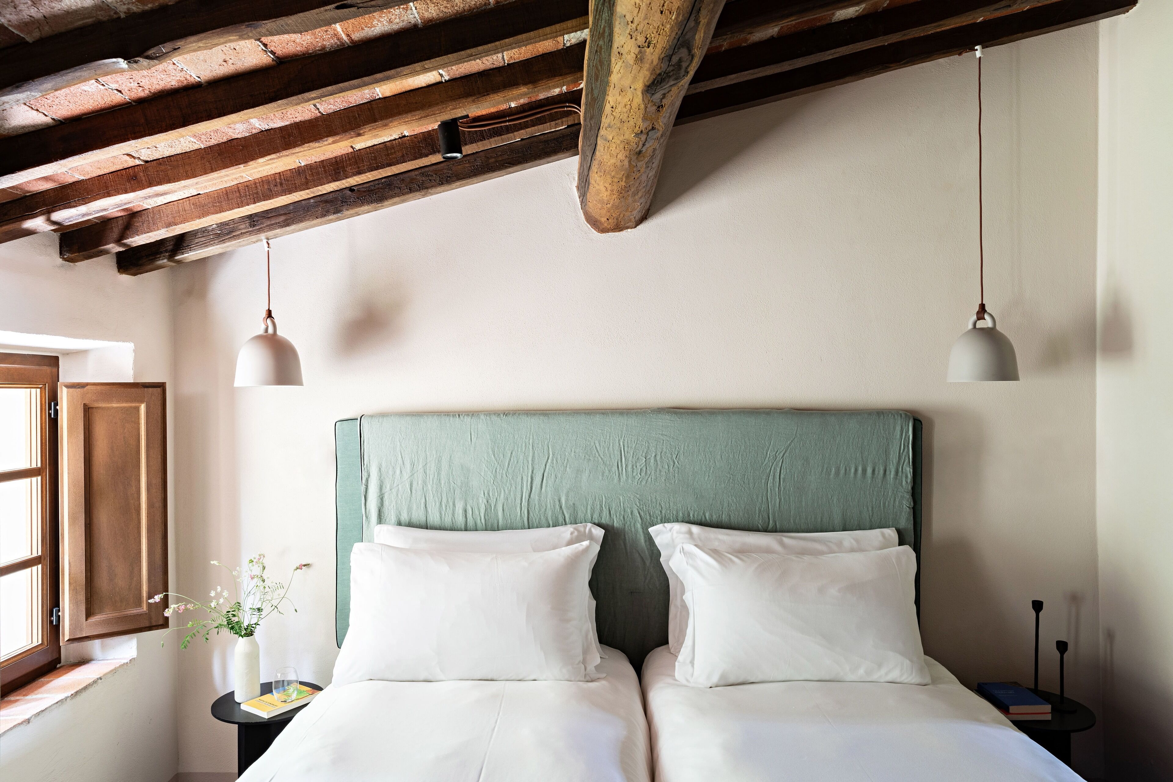Una stanza con un letto, un comodino, una finestra e una lampada a sospensione.
