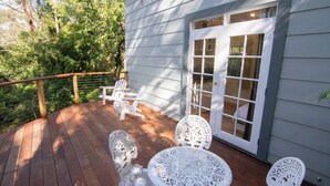 A wooden deck with white outdoor furniture, including chairs and tables, and a door with glass panels.