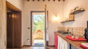 Une cuisine avec une porte en bois, un plan de travail rouge, un évier et une fenêtre donnant sur un jardin.