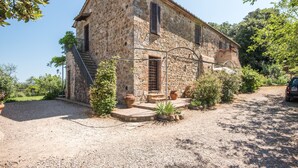 Un bâtiment en pierre avec une allée gravillonnée, un petit jardin agrémenté de plantes en pot et un escalier menant à un étage supérieur.