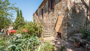 Un bâtiment en pierre avec un escalier menant à une porte, le tout entouré de verdure et de fleurs.
