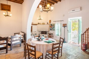 A dining area with a round table, chairs, a chandelier, and a fireplace.
