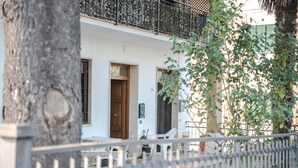 Un edificio blanco con un balcón, una puerta de madera y una silla blanca en el exterior.