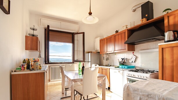 Una cocina con armarios de madera, una estufa a gas, una mesa de comedor blanca con sillas y vistas por una ventana.